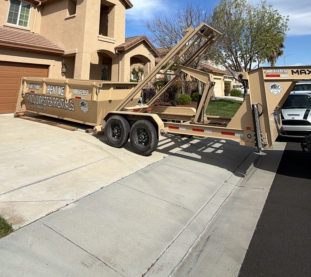 Tan RM Dumpster Rentals roll-off container being set down in a residential driveway